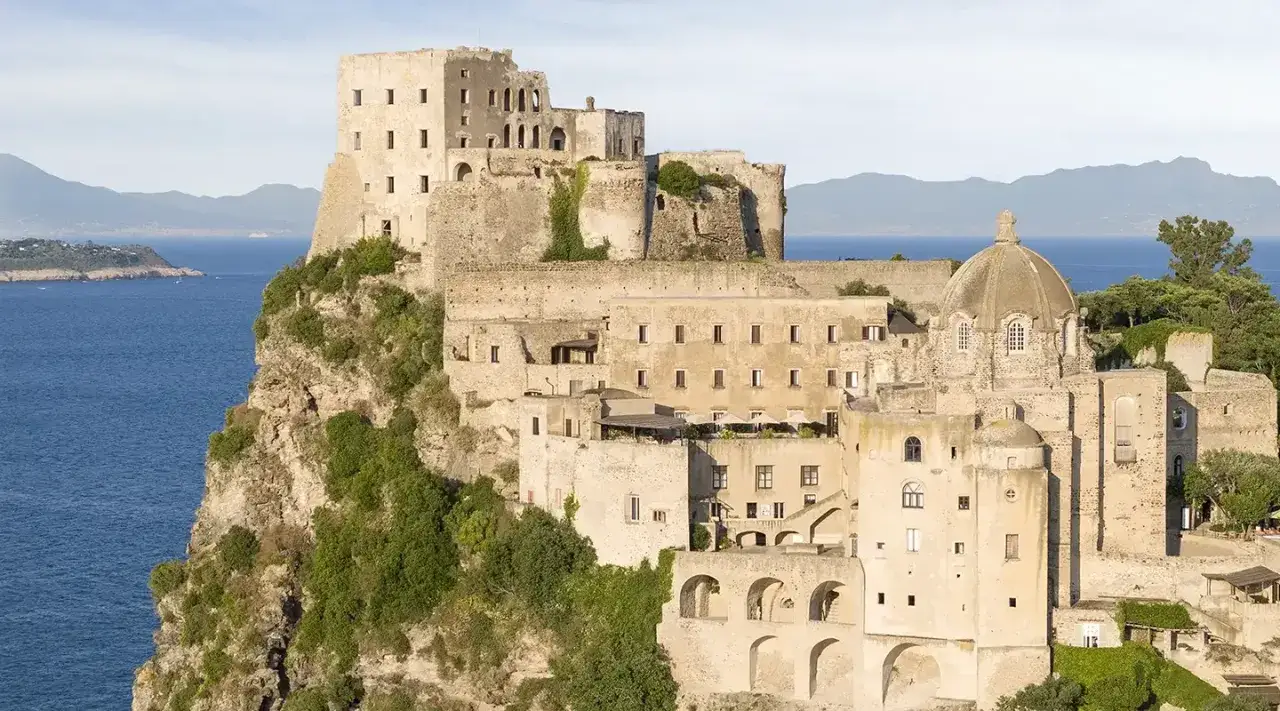 Antico albergo il monastero arroccato su una scogliera a picco sul mare blu, con cupola e torri imponenti.