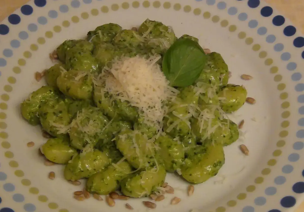 Pyszne gnocchi z pesto, posypane parmezanem i orzeszkami pinii, ozdobione listkiem bazylii.