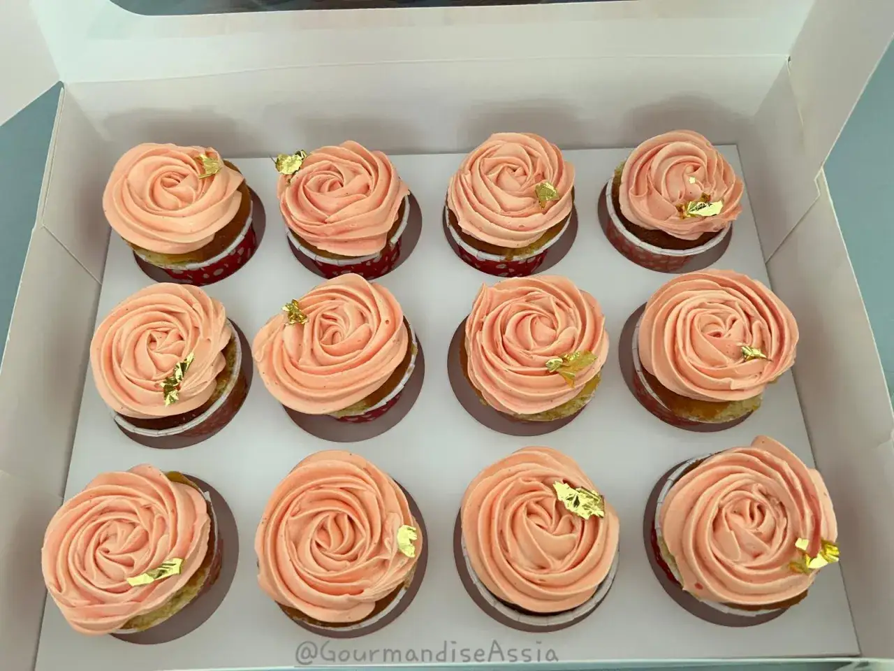 Douze cupcakes décorés d'une délicate crème au beurre, saupoudrés de sucre glace et de feuilles d'or comestibles.