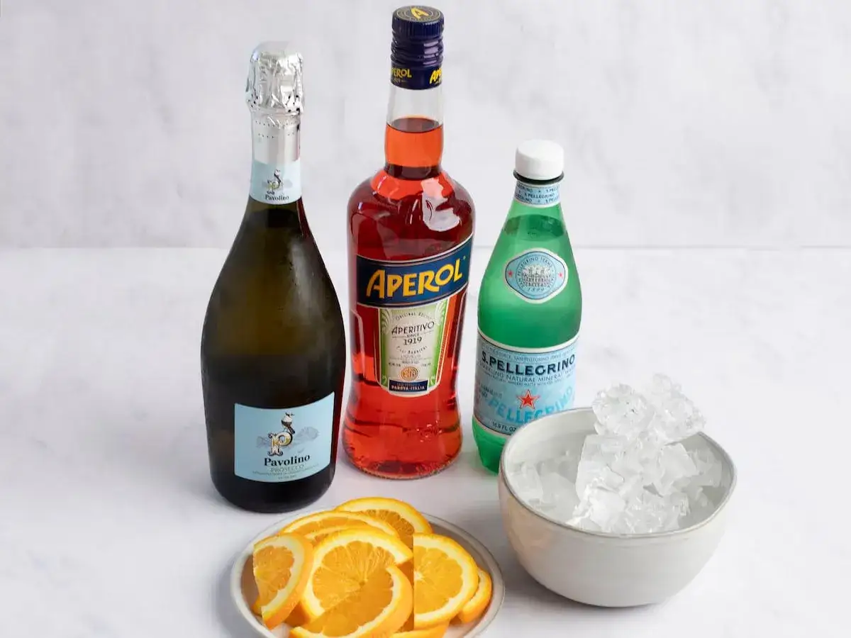 Składniki na Aperol Spritz: butelka prosecco, Aperol, woda gazowana, plasterki pomarańczy i lód. Idealne aperol proporcje.