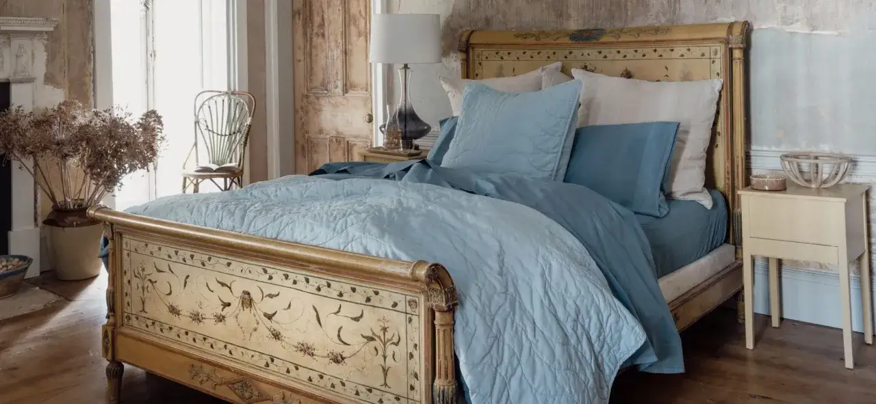 A rustic bedroom with a vintage bed, featuring two blue shams and a quilted coverlet.
