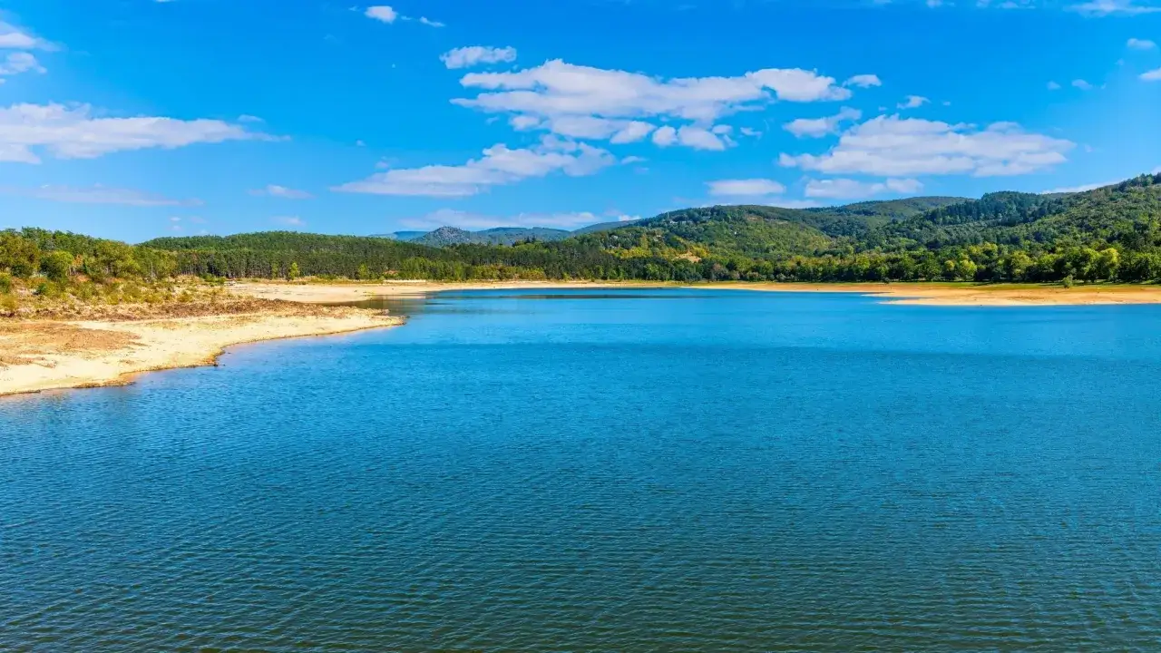 Vaste lac aux eaux bleues vives, bordé de rives sablonneuses et de collines verdoyantes. Un paysage paisible près de Toulouse.