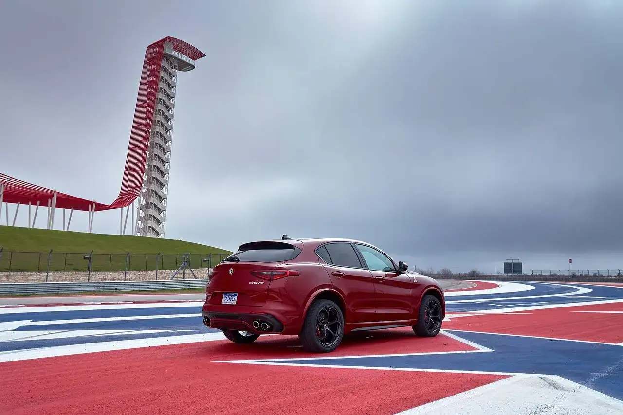 Czerwone Alfa Romeo Stelvio Quadrifoglio na torze wyścigowym, z charakterystyczną wieżą widokową w tle.