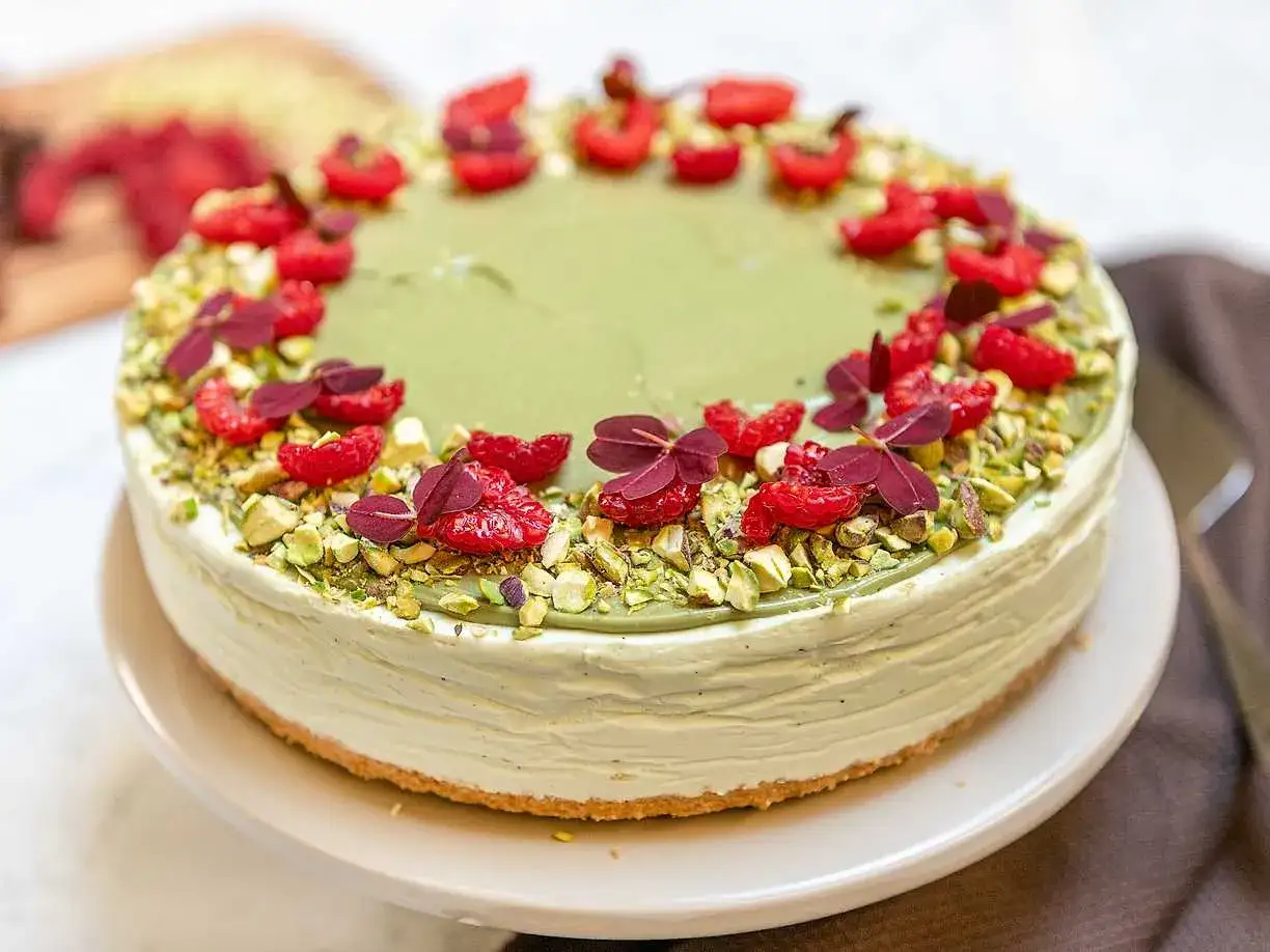 En läcker pistage cheesecake med hallon och nötter.