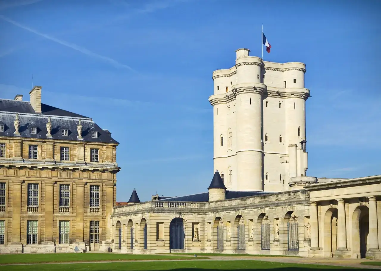 Le **ch&acirc;teau de Vincennes** se dresse fi&egrave;rement sous un ciel bleu, avec sa tour imposante et ses b&acirc;timents historiques.