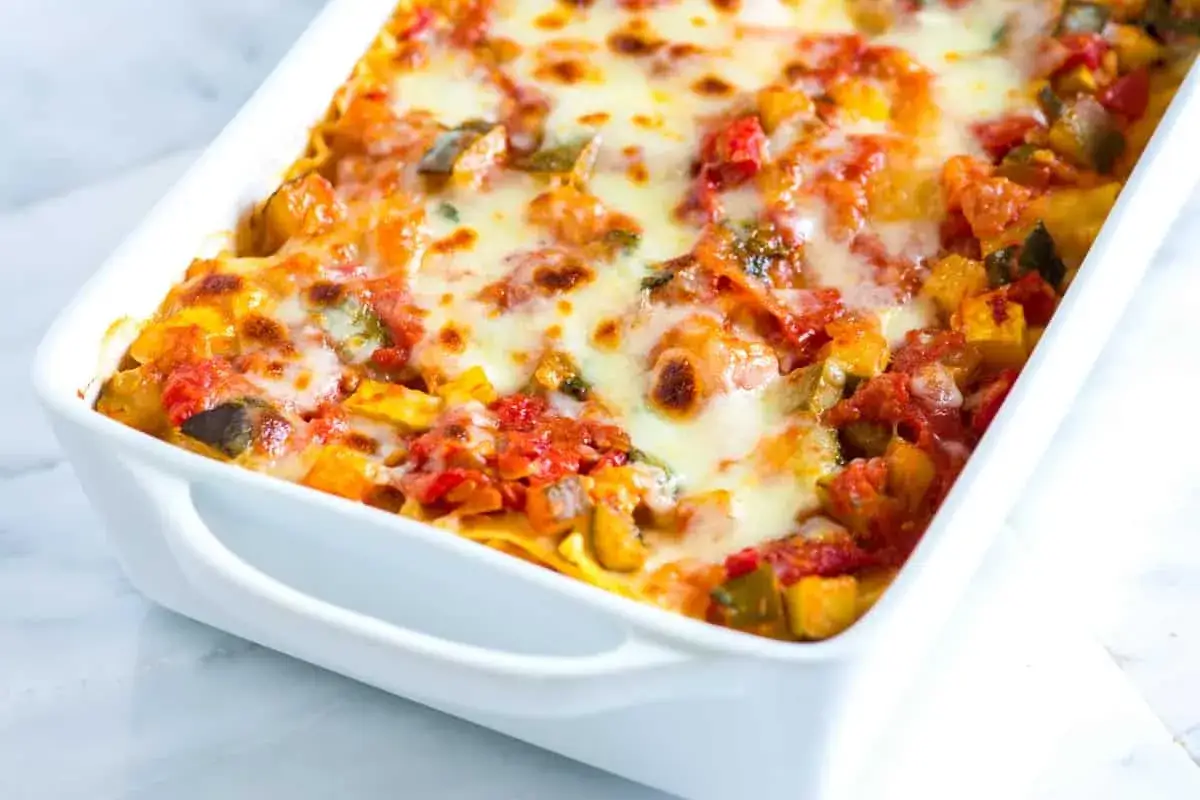 Lasaña de verduras recién horneada, con capas de pasta, tomate y queso derretido burbujeante.