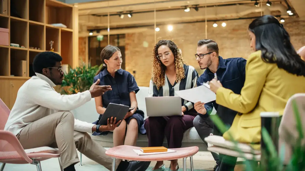 Une équipe discute autour d'un ordinateur portable, illustrant la **plateforme collaborative définition** et le travail d'équipe moderne.