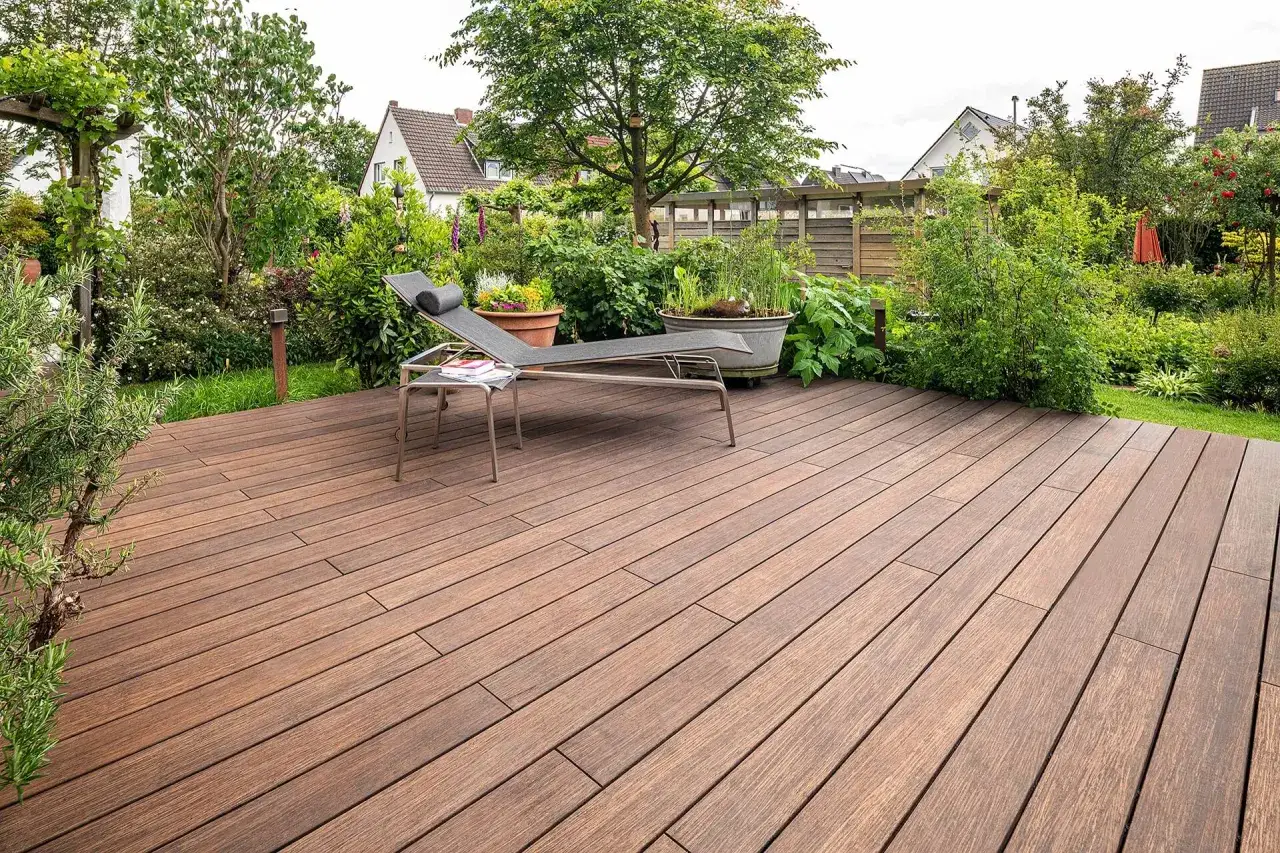 Une chaise longue attend sur une belle terrasse sur plot bois, entourée d'un jardin luxuriant.