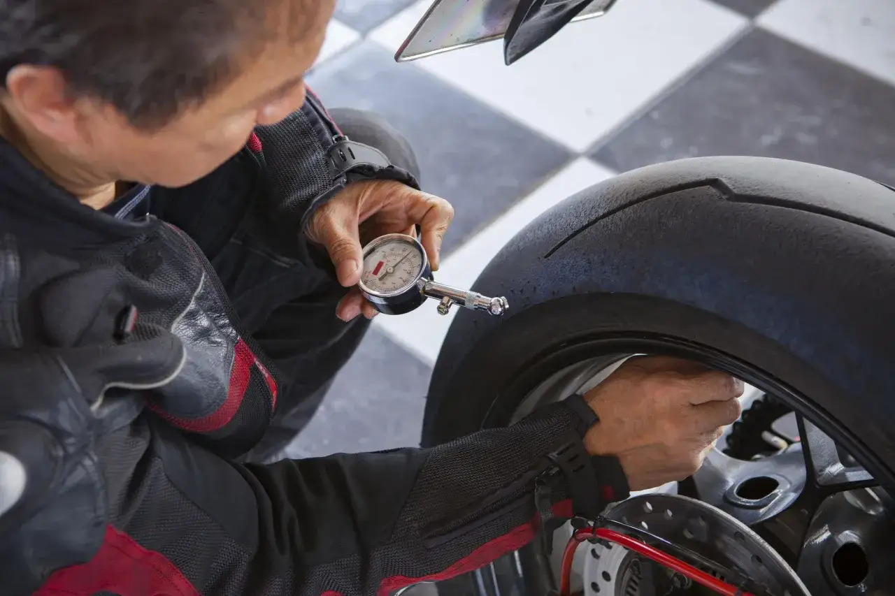 Uomo in tuta da moto controlla la pressione gomme moto con un manometro.