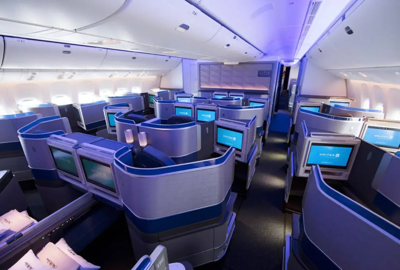 Luksusowa klasa biznes w samolocie United Polaris. Fotele z ekranami i niebieskimi akcentami tworzą komfortową przestrzeń podróży.