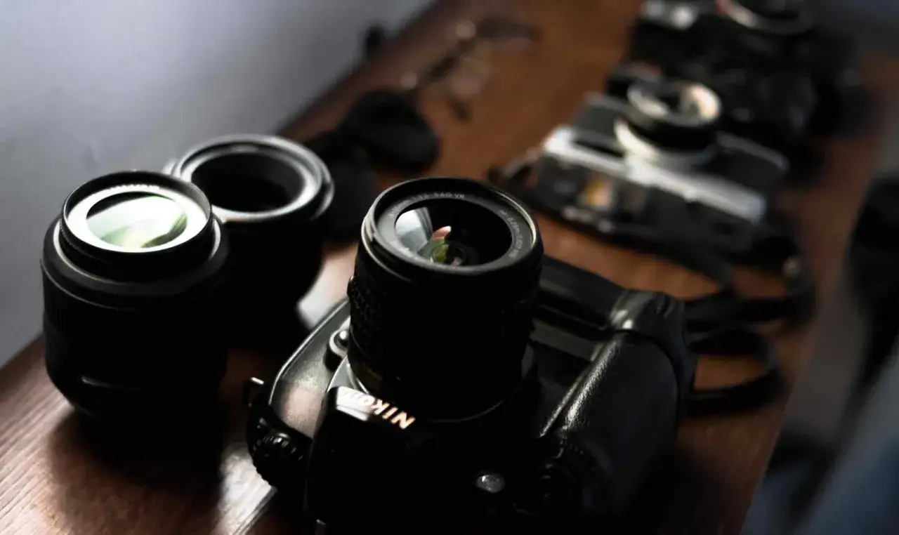 Obiektywy i aparaty Nikon na drewnianym blacie. Widać szczegóły, jakbyśmy patrzyli w **skala makro**.