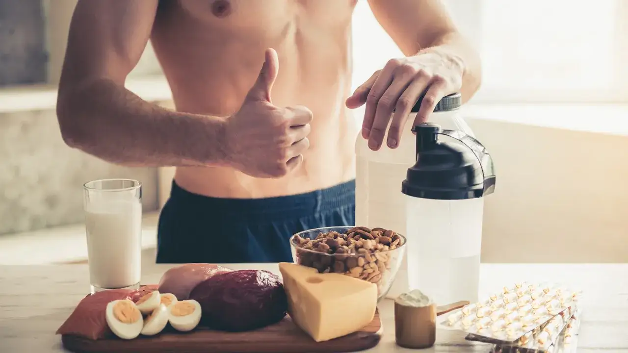 Mann gibt Daumen hoch neben Proteinshakes und Lebensmitteln wie Fisch, Fleisch, Eiern und N&uuml;ssen. Was ist Eiklar? Eine gute Proteinquelle f&uuml;r Sportler.