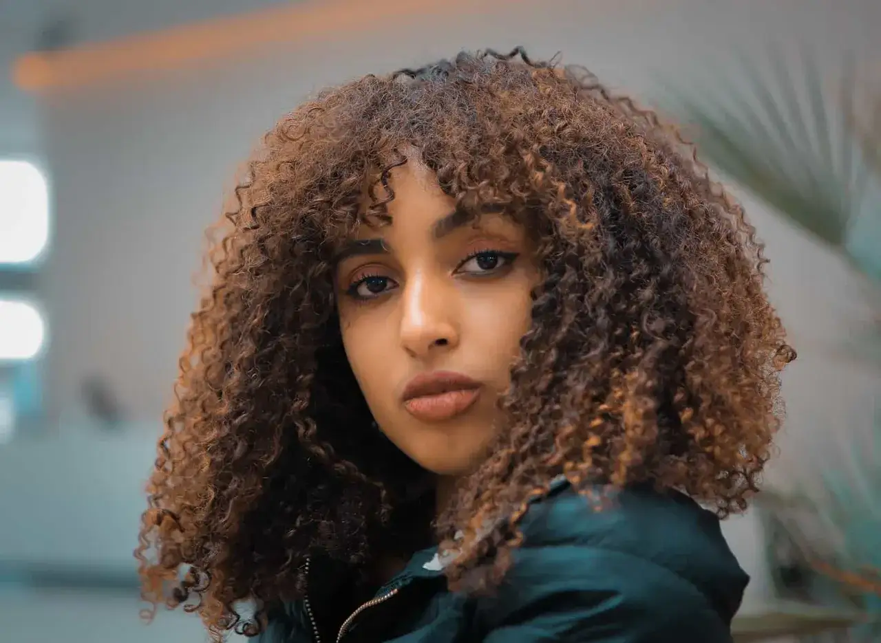 Mujer joven con cabello rizado y voluminoso, un estilo que realza su belleza natural.
