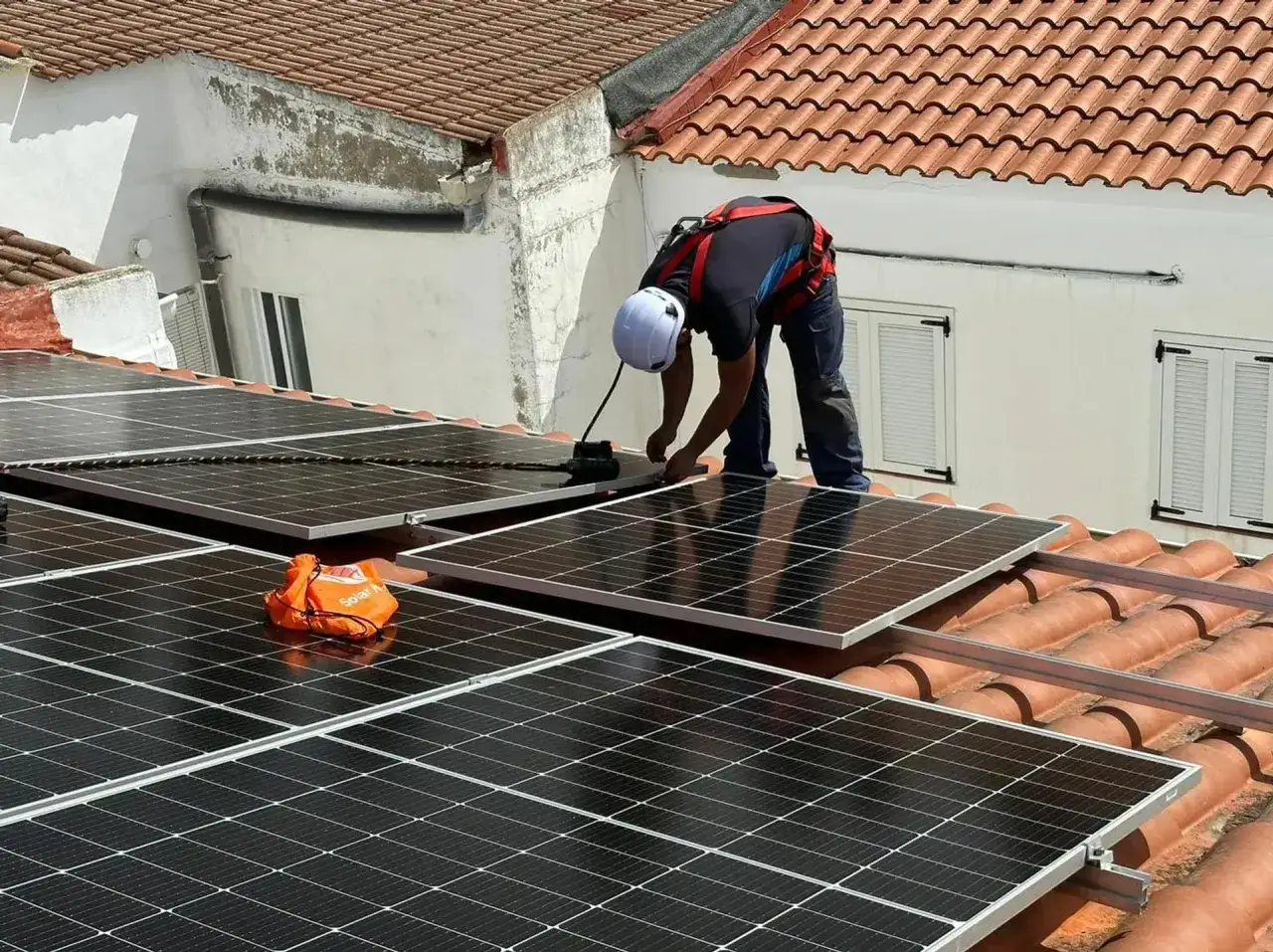 Instalaci&oacute;n de placas solares en Extremadura. Un t&eacute;cnico con arn&eacute;s trabaja en un tejado, asegurando paneles fotovoltaicos.
