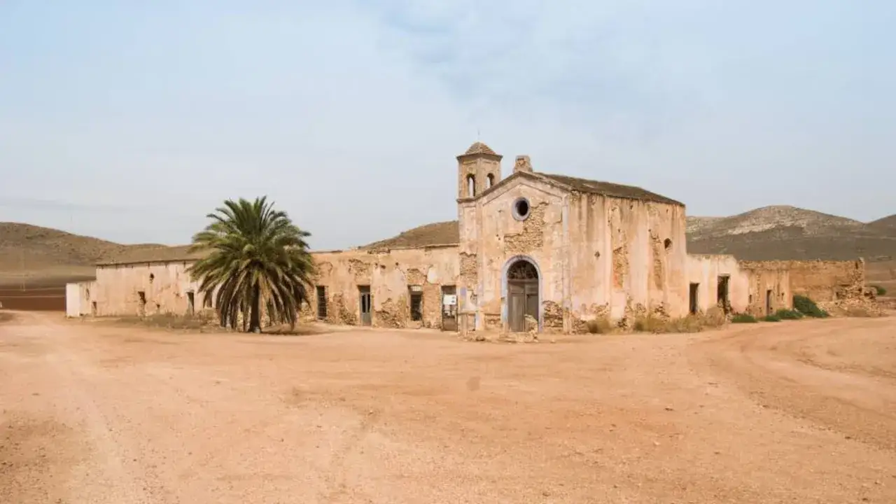 El cortijo del fraile, una edificación en ruinas con una torre campanario, se alza desolado en un paisaje árido, con una palmera solitaria.
