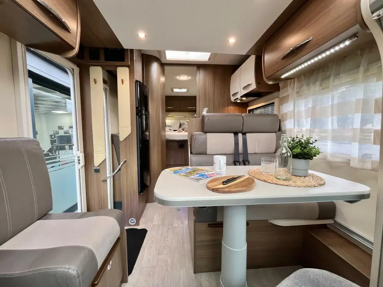 Int&eacute;rieur d'un camping-car Chausson 628 EB : salon cosy avec table, si&egrave;ges confortables et vue sur la chambre. Avis camping-car.