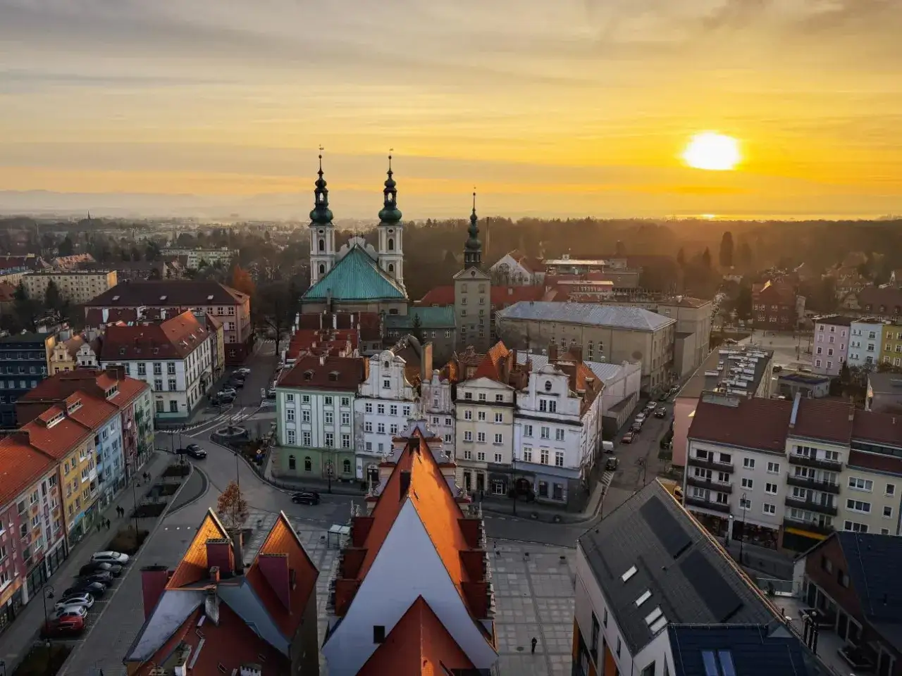 Zach&oacute;d słońca nad Nysą. Widok z g&oacute;ry na zabytkowe kamienice i kości&oacute;ł z wieżami. Trasa przez miasto oświetlona złotym blaskiem.