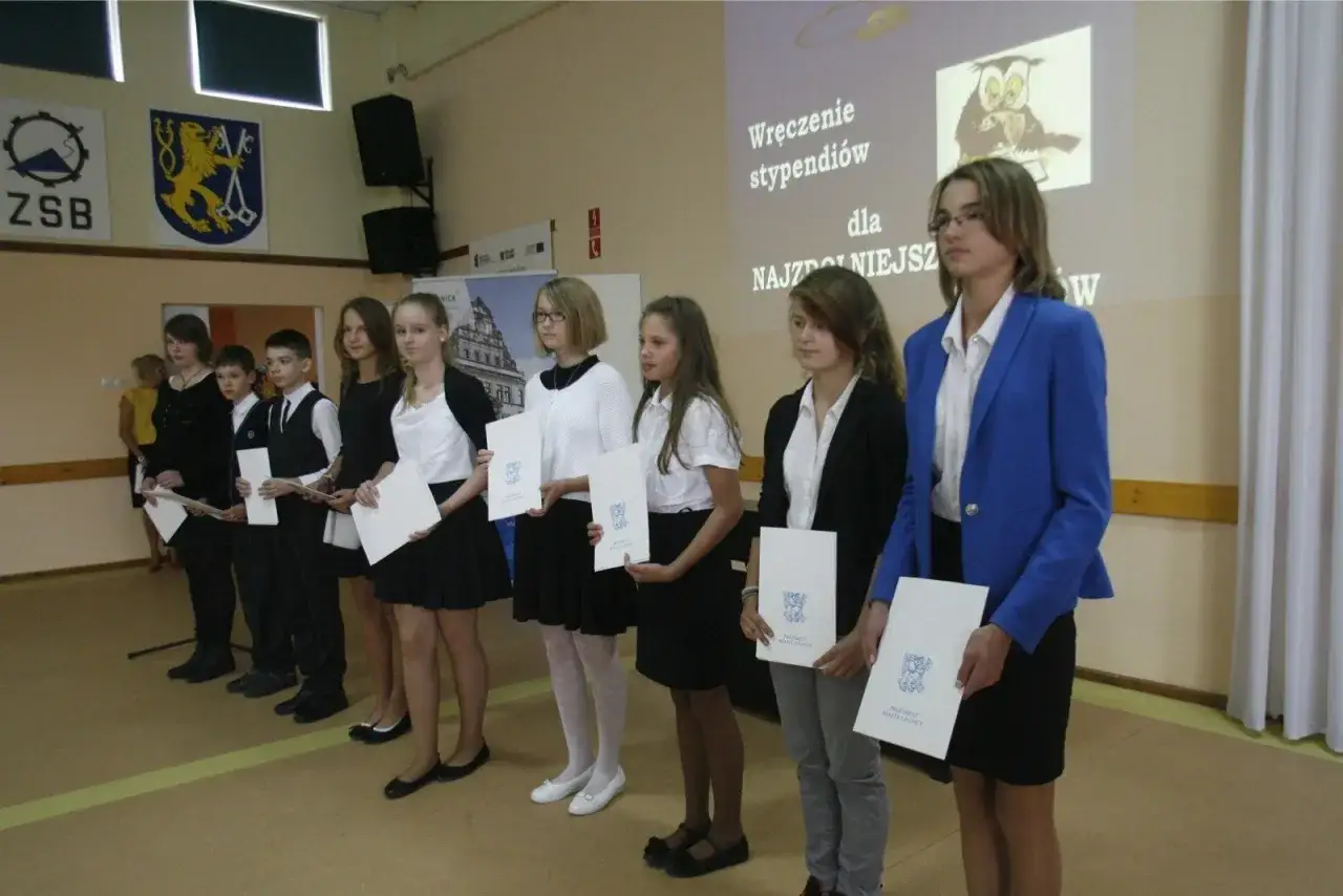 Uczniowie w eleganckich strojach, jak się ubrać na zakończenie roku szkolnego, odbierają dyplomy.