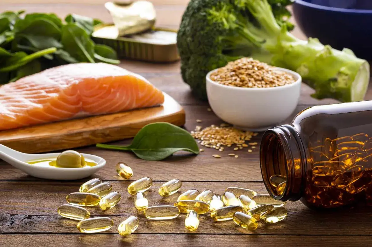 Łosoś, szpinak, brokuły i nasiona lnu &ndash; naturalne źr&oacute;dła kwas&oacute;w omega 3. Obok leżą kapsułki z suplementem.