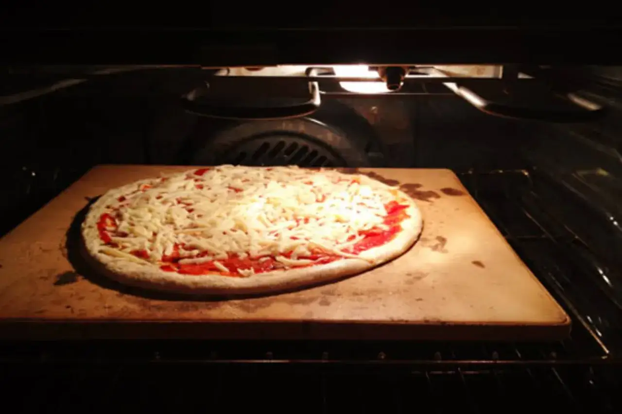 Rohe Pizza mit Tomatensauce und viel Käse auf einem Pizzastein im Ofen, bereit zum Backen.