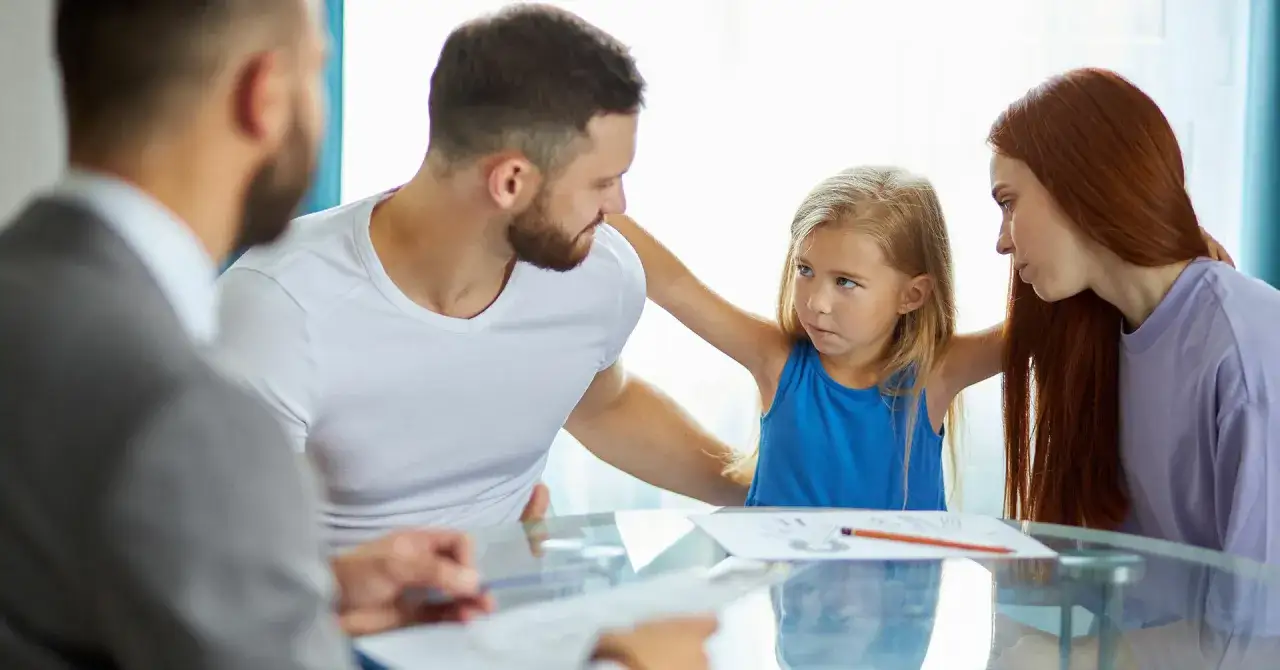Ein besorgtes Kind sitzt zwischen Vater und Mutter, während ein Anwalt Papiere reicht. Eine schwierige Situation, vielleicht eine Trennung in der Schwangerschaft.