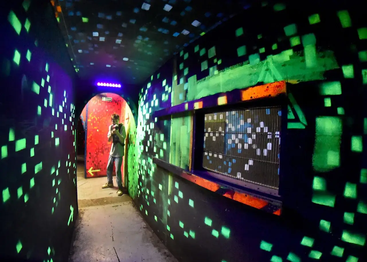 Laser tag arena z neonowymi światłami i kwadratowymi wzorami na ścianach. Idealne miejsce dla młodzieży szukającej rozrywki w Krakowie.