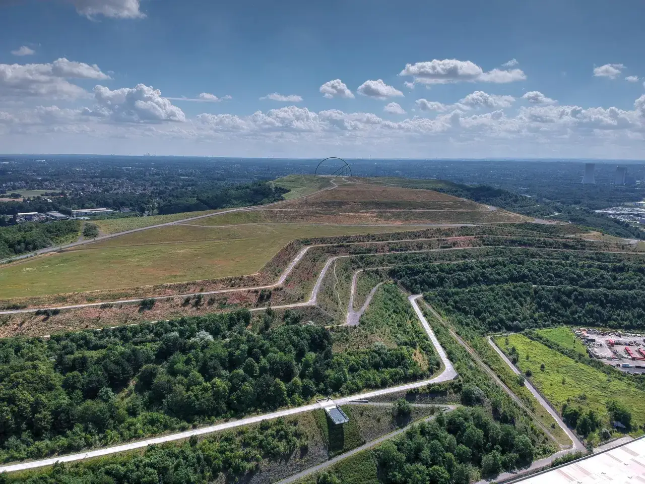 Weite Landschaft mit geschwungenen Wegen, ideal für eine Fahrradtour in Recklinghausen. Im Hintergrund ragt eine markante Skulptur auf.