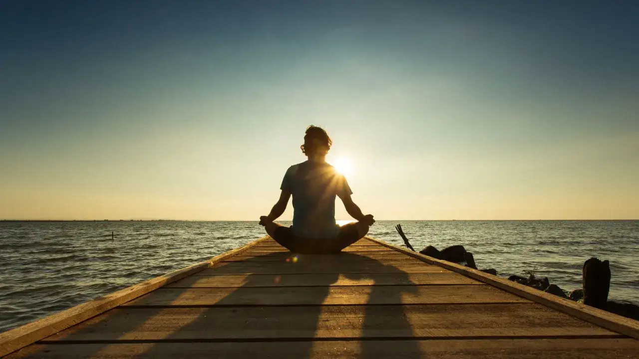 Silueta de persona meditando en un muelle al atardecer. Aprende como meditar y encuentra paz.