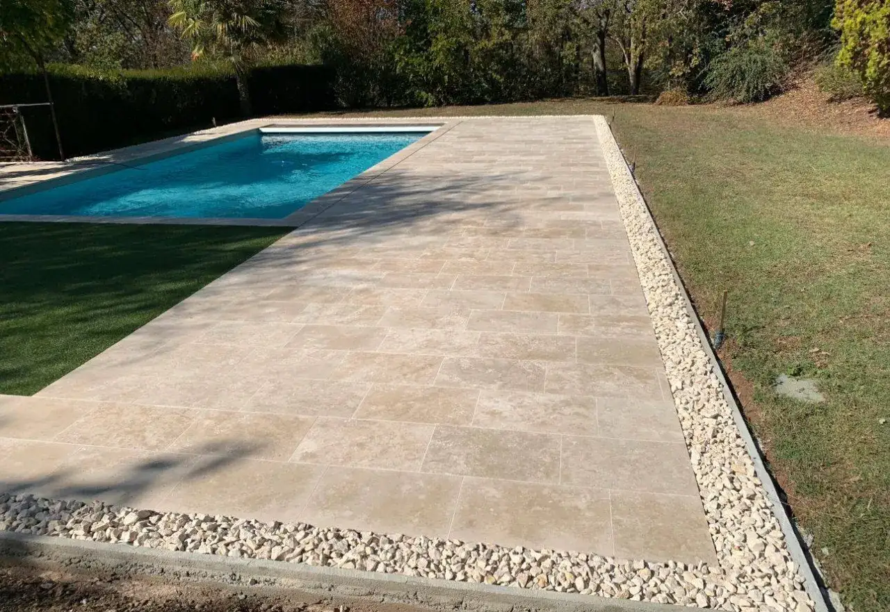 Une belle terrasse en travertin, avec une piscine et une pelouse. Avis positifs pour ce revêtement naturel et résistant.