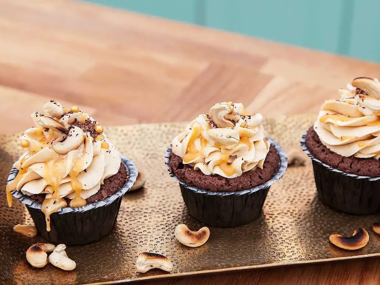 Kladdmuffins med chokladkola, toppade med krämig frosting, cashewnötter och kolasås. En dröm för alla chokladälskare!
