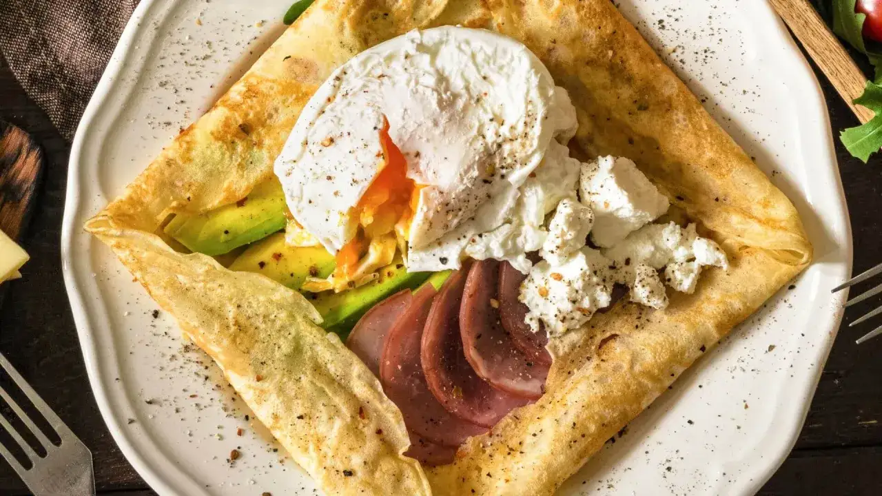 Crêpe au fromage garnie d'un œuf poché coulant, d'avocat, de jambon et de fromage frais. Un délice pour le petit-déjeuner.
