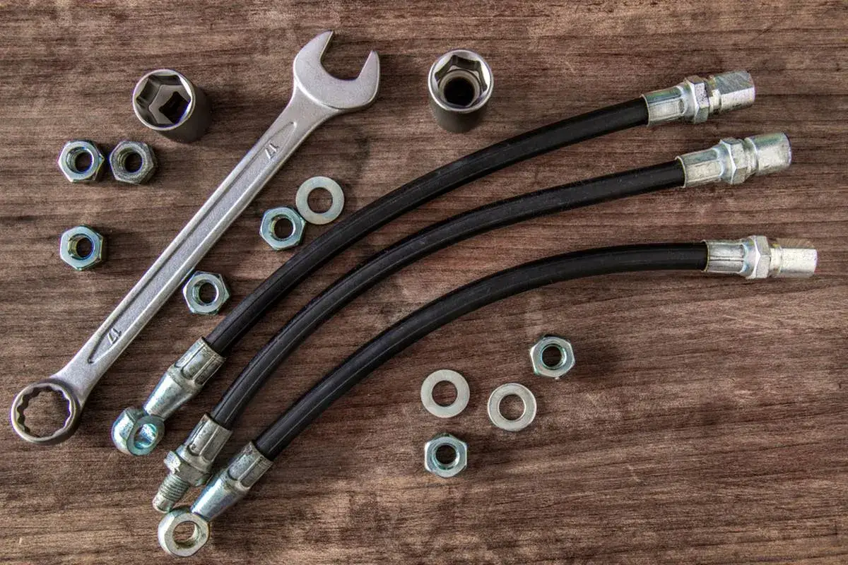 Ensemble d'outils et de pièces pour un système de freinage, incluant des flexibles de frein endommagés, des écrous, des rondelles et une clé.