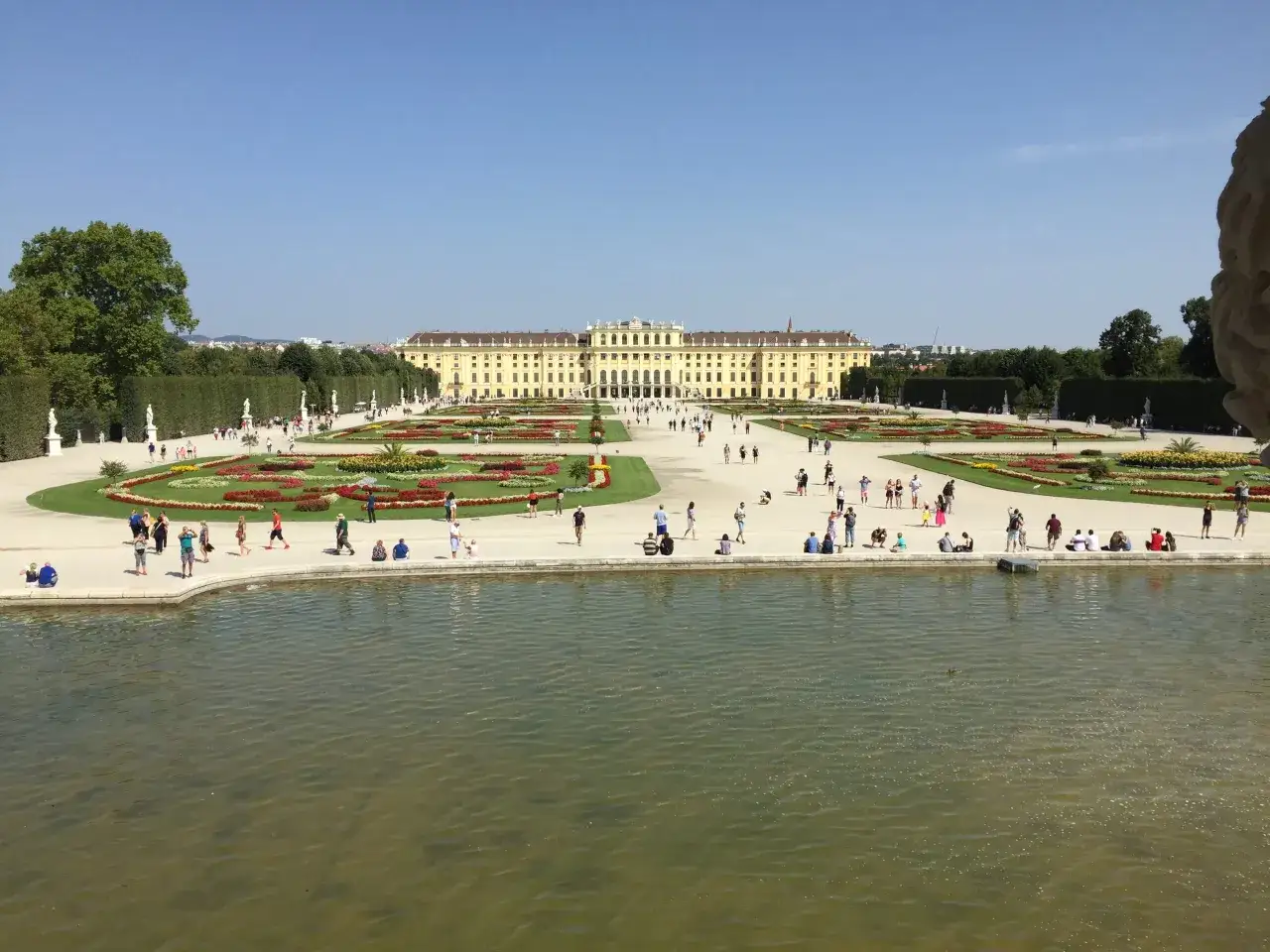 Wiedeń w jeden dzień: Pałac Sch&ouml;nbrunn i jego ogrody, z turystami spacerującymi pośr&oacute;d kwiatowych rabat i przy stawie.