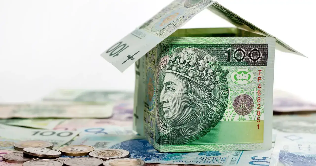 Domek z banknotów 100 zł, symbolizujący inwestycję, co nie może być wkładem własnym. Monety i inne banknoty w tle.