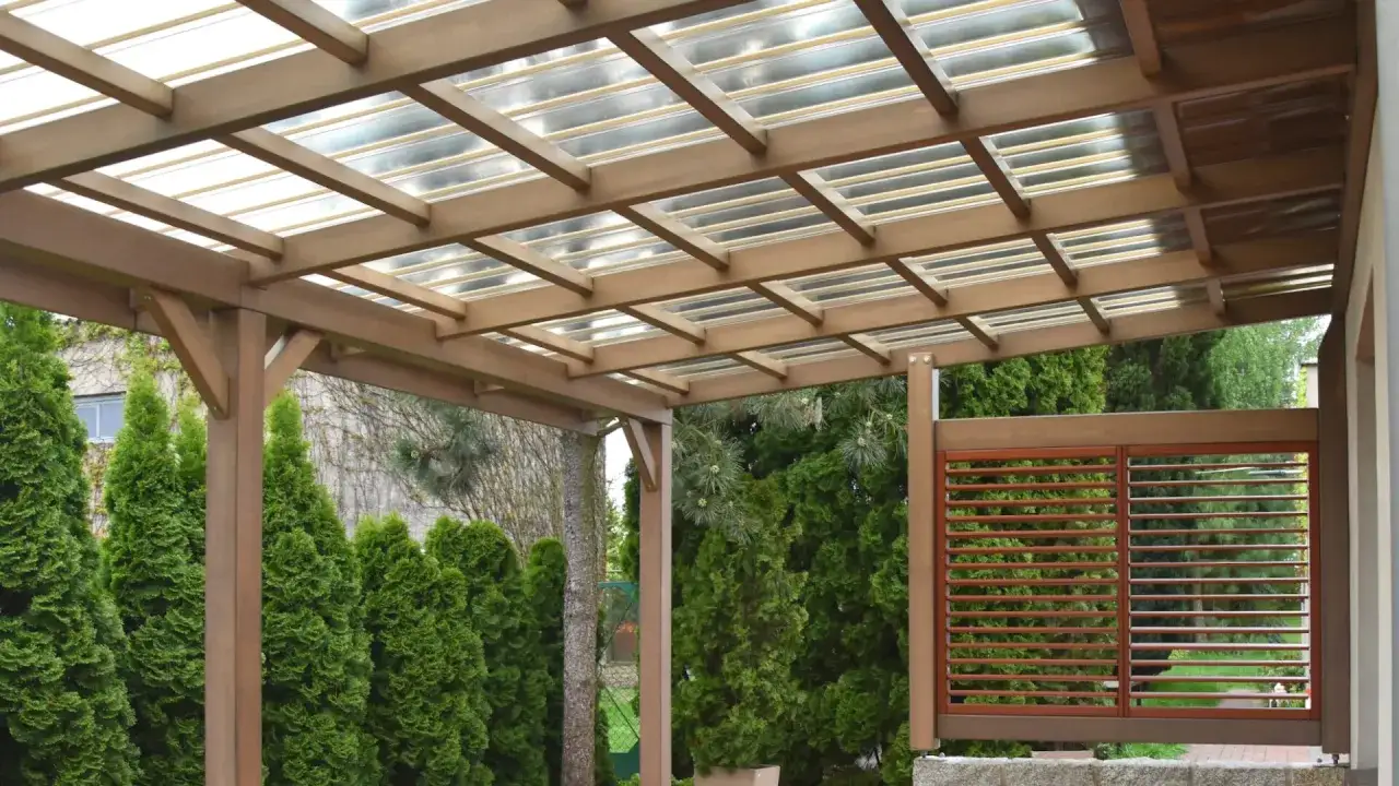Drewniana pergola z przezroczystym dachem, idealna na co na dach pergoli. Otoczona zielenią, z ozdobną kratownicą.