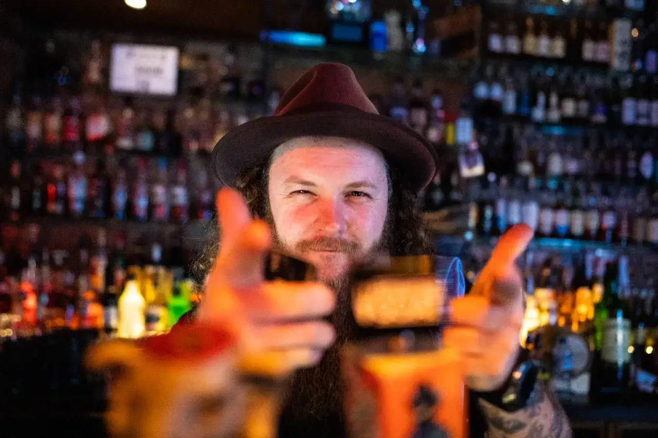 Mężczyzna w kapeluszu i z brodą, w tle bar z butelkami. Test aparatu sony a7 iii.