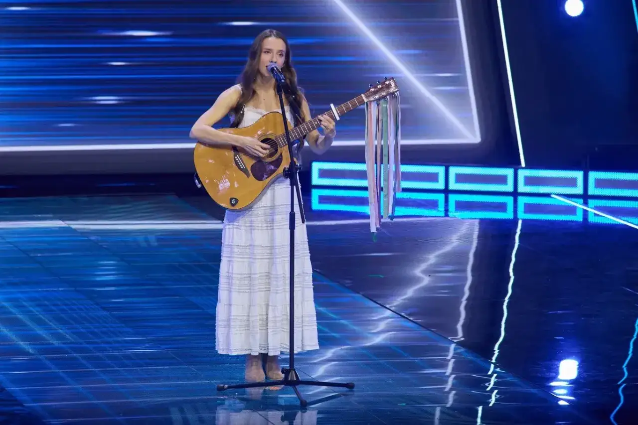 Dziewczyna z gitarą na scenie, śpiewająca. Jej stylizacja i występ mogą inspirować, jak zostać piosenkarką.