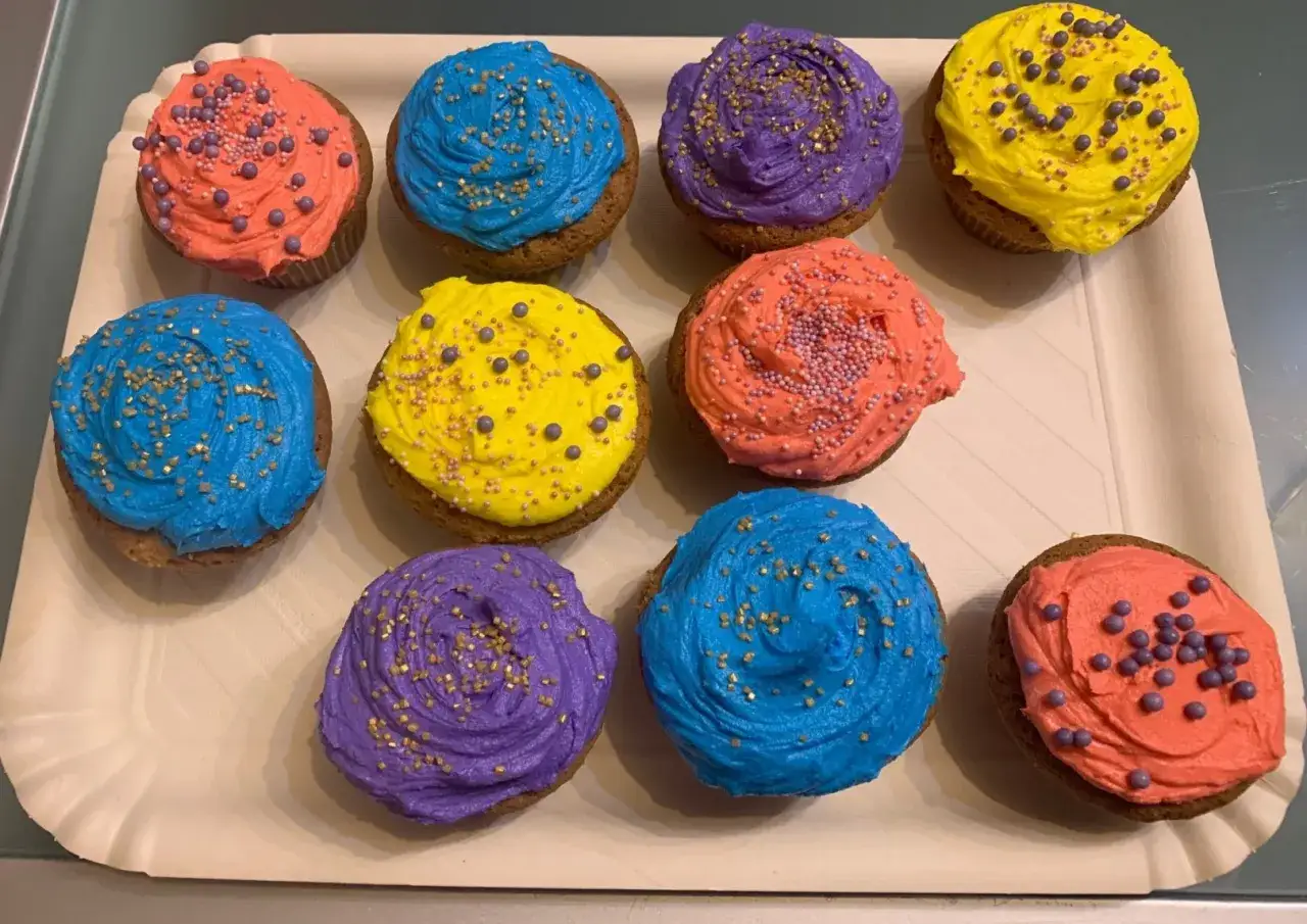 Dieci cupcake colorati con crema al burro, decorati con zuccherini dorati e perline viola.