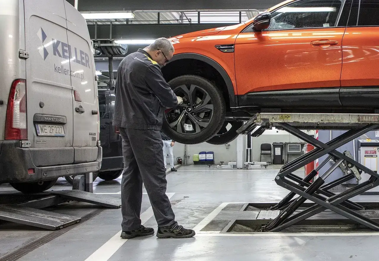 Mechanik sprawdza koło pomarańczowego auta na podnośniku. Zastanawiasz się, ile kosztuje wymiana opon?