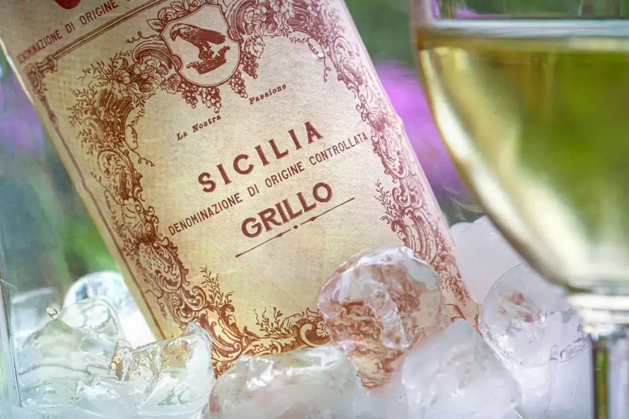 Butelka wina Grillo z Sycylii schłodzona w lodzie, obok kieliszek białego wina.