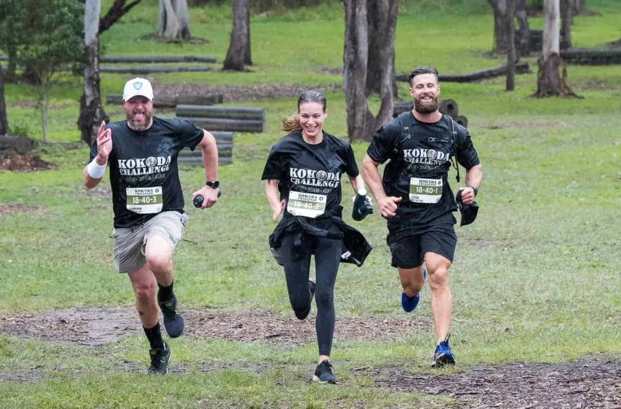 Drei L&auml;ufer trainieren bei Regen f&uuml;r die Kokoda Challenge. Sie tragen schwarze T-Shirts mit der Aufschrift 