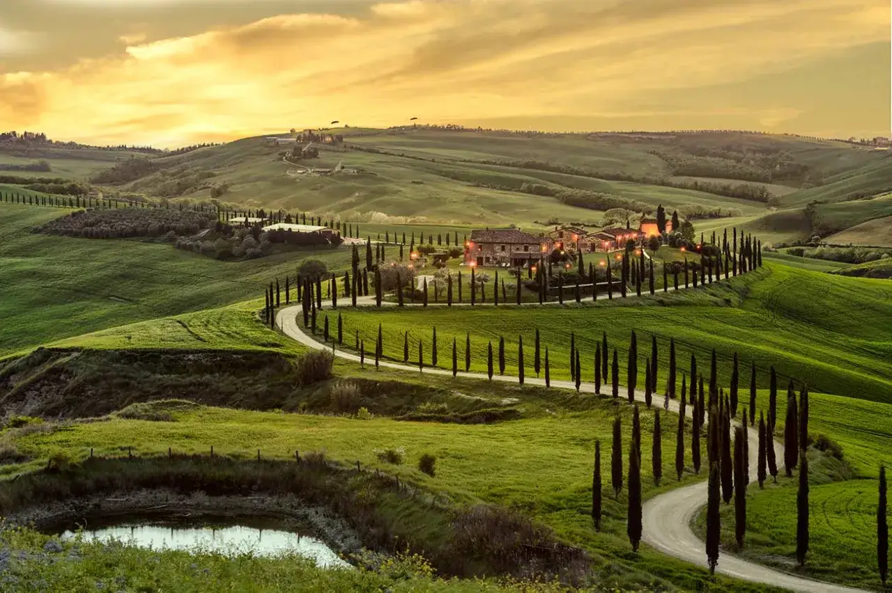 Colline toscane al tramonto, con cipressi che fiancheggiano una strada tortuosa verso un casale. Perfetto per scoprire cosa vedere a Siena e dintorni in 3 giorni.
