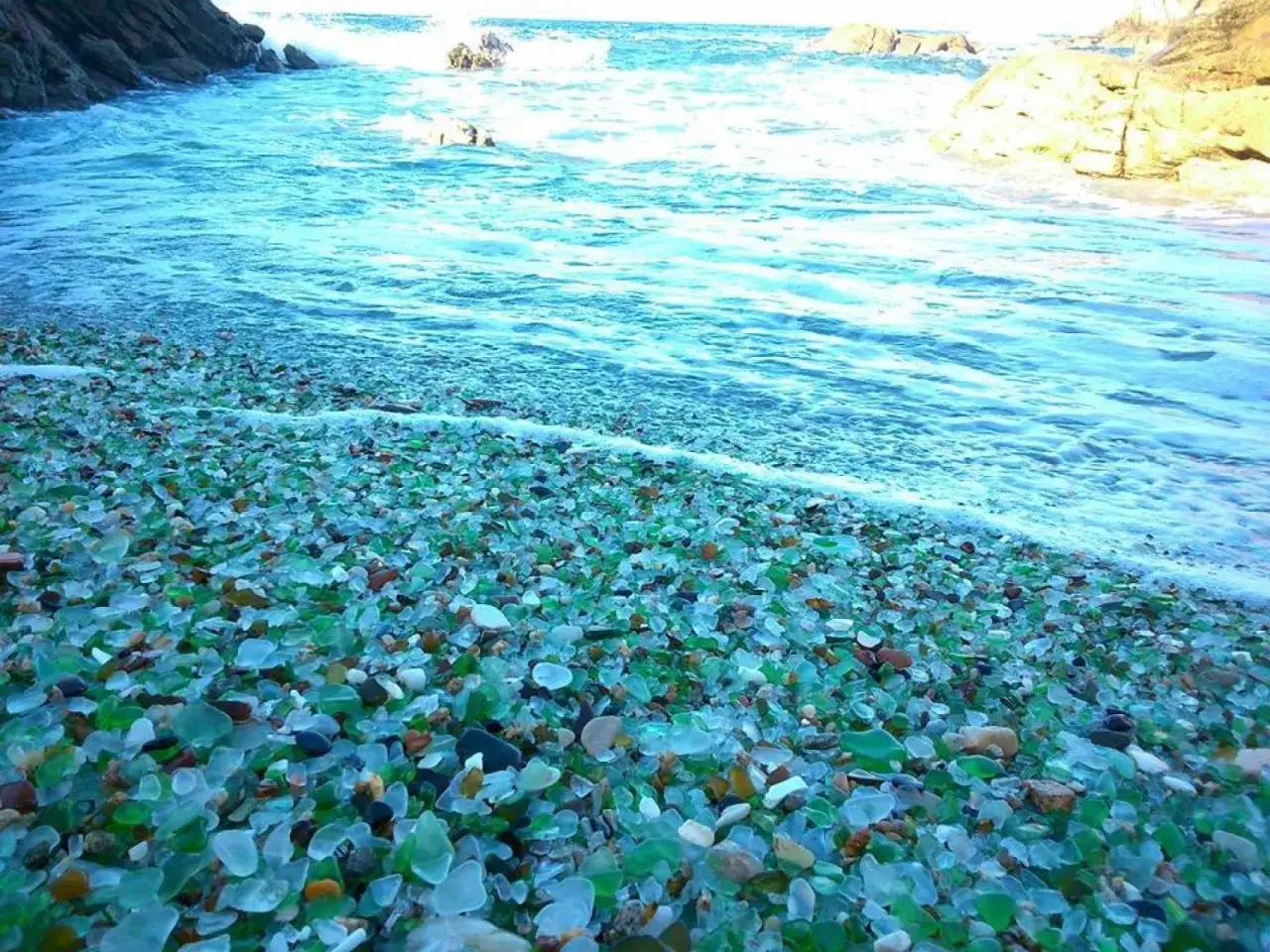 La **praia dos cristais** brilla con miles de fragmentos de vidrio pulido por el mar, mezclados con guijarros, mientras las olas acarician la costa.