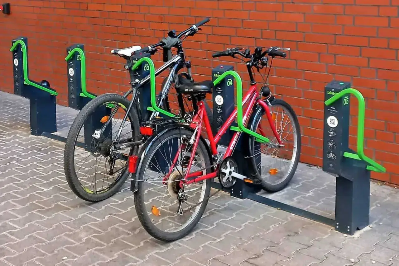 Dwa rowery, czarny i czerwony, przypięte do zielonego stojaka rowerowego. Prosty spos&oacute;b, jak przypiąć rower do stojaka.
