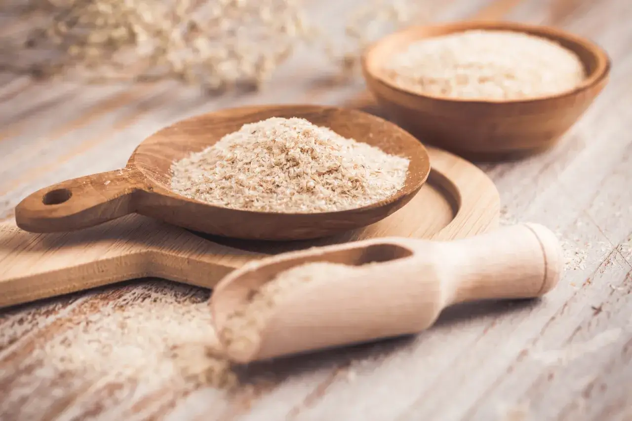 Cuill&egrave;res en bois remplies de psyllium blond, une poudre l&eacute;g&egrave;re et naturelle, sur une planche en bois.