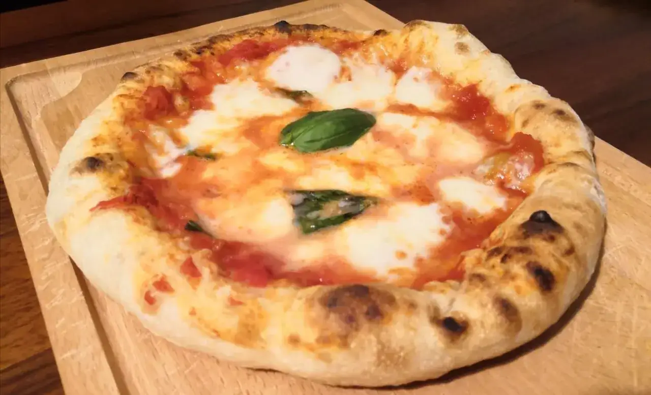 Pizza in padella, appena sfornata, con pomodoro, mozzarella filante e basilico fresco su un tagliere di legno.