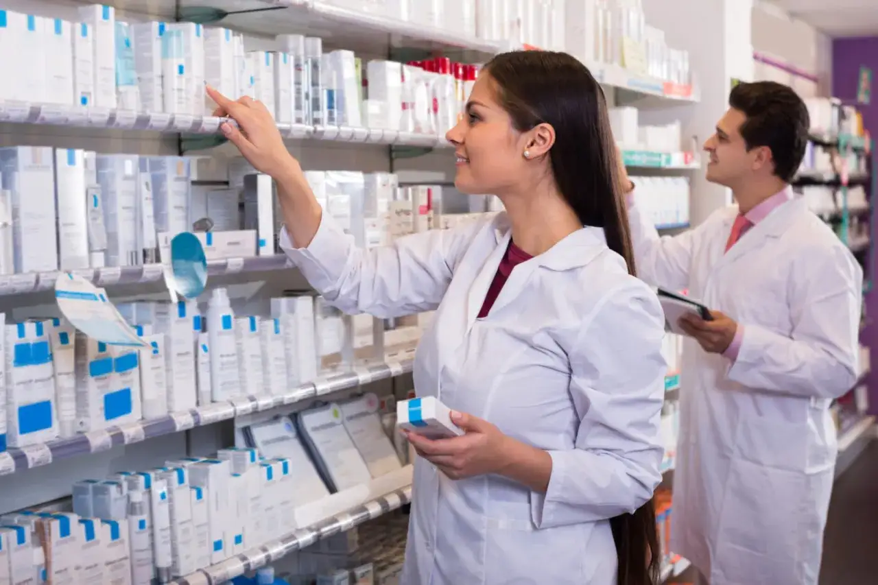Farmacéuticos en un estante de productos, uno revisa un producto, otro toma notas. Futuros profesionales del grado superior de farmacia.