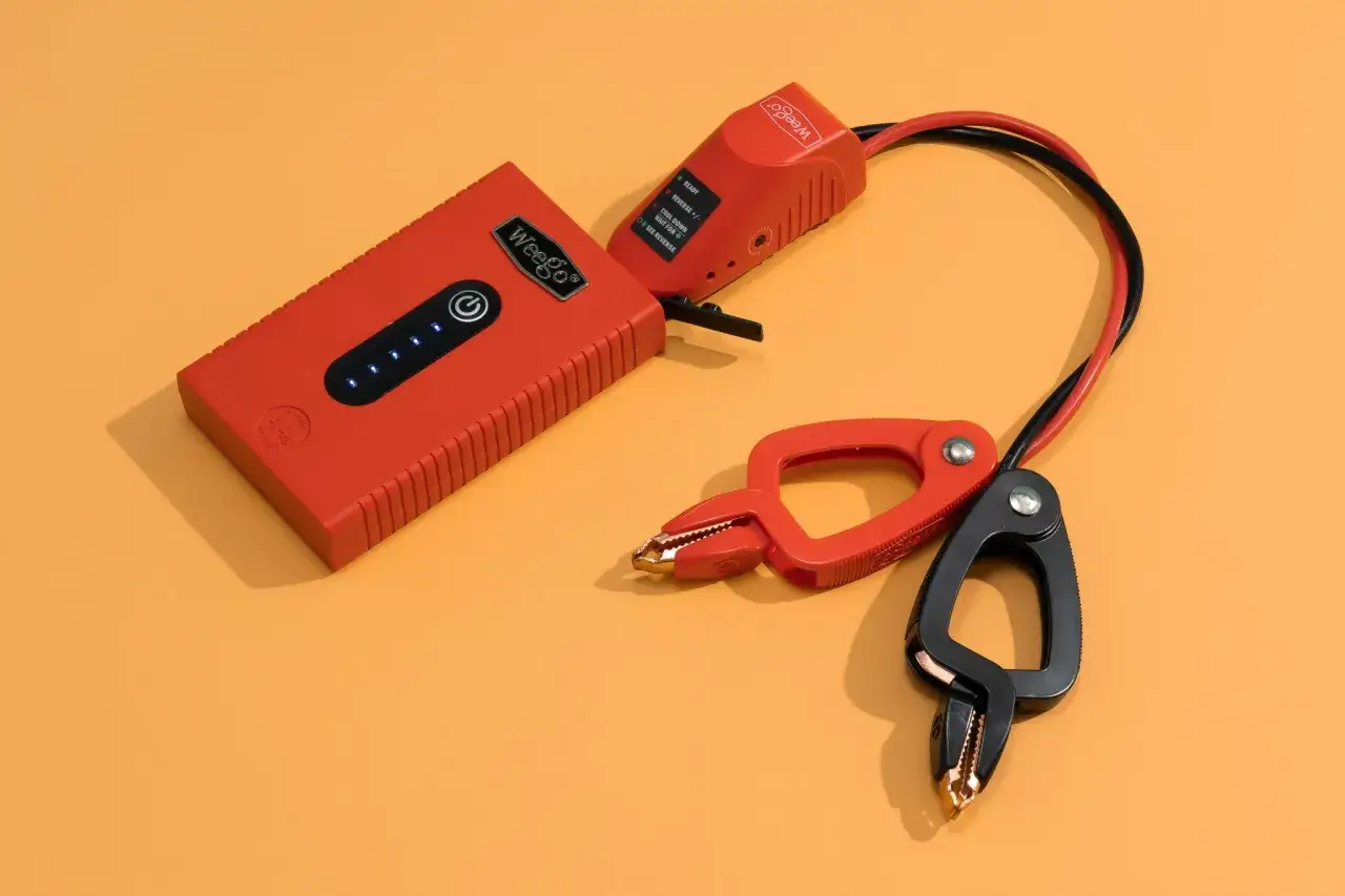 A red jump starter with cables and clamps. Learn how to charge jump starter without charger for emergency power.
