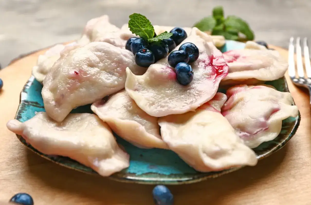 Pyszne pierogi z bor&oacute;wkami amerykańskimi, ozdobione świeżymi owocami i miętą, czekają na talerzu.