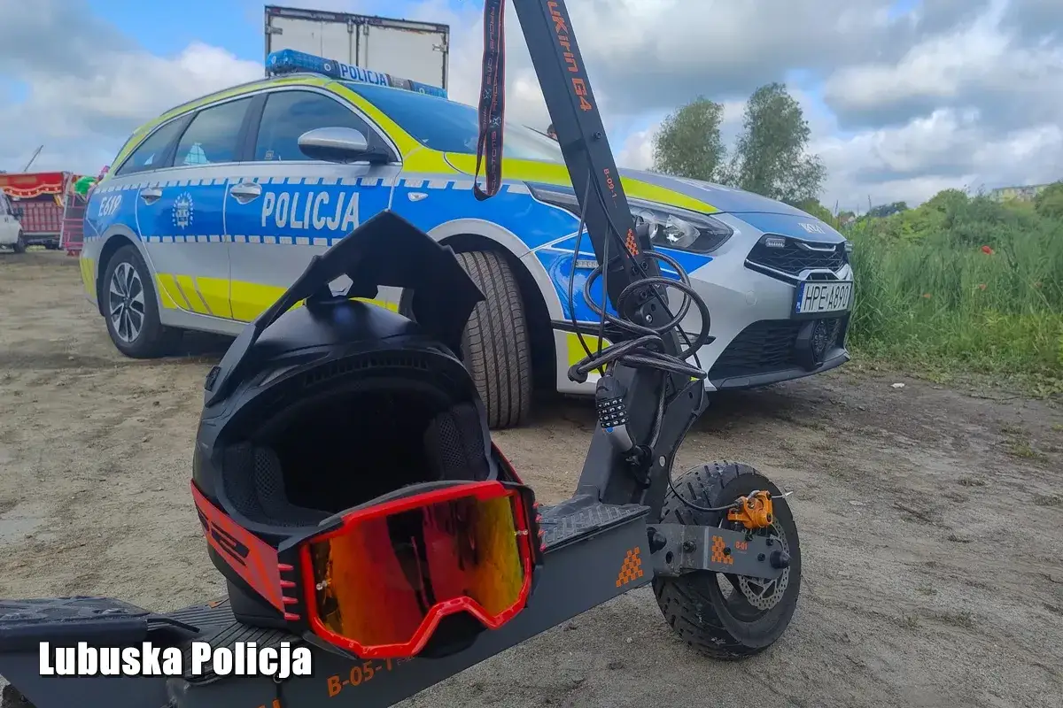 Kask i gogle na hulajnodze, obok radiowozu policyjnego. Lubuska Policja przypomina o bezpieczeństwie w ruchu drogowym, także przy korzystaniu z urządzeń transportu osobistego.